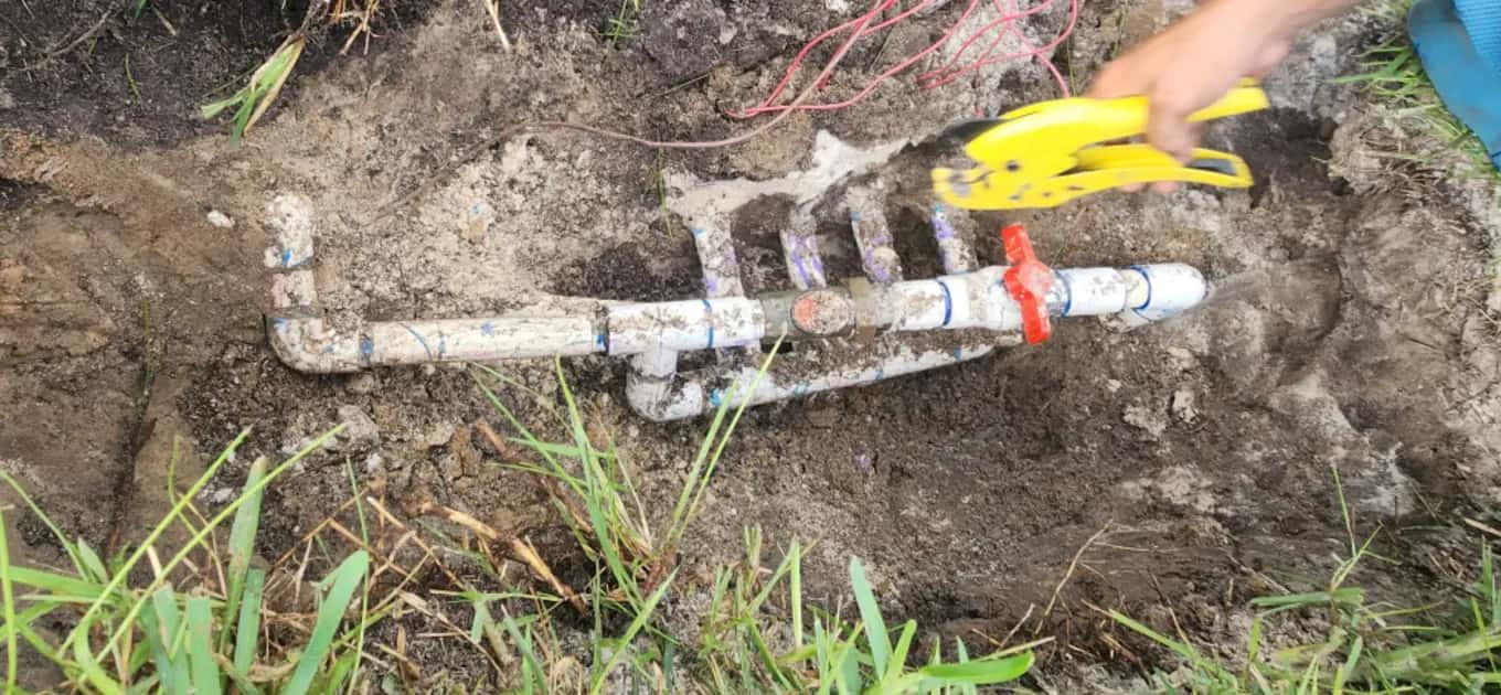 Technician cutting PVC pipe while rebuilding a sprinkler valve manifold in an open trench