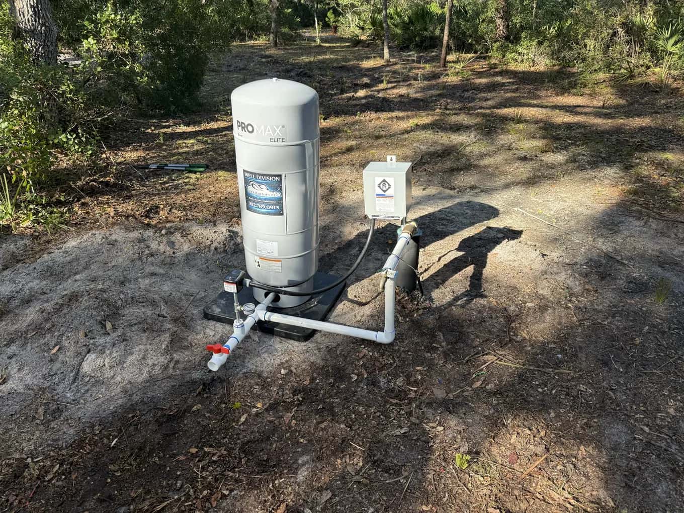 New well pressure tank and pump control box installed on a pad in a wooded yard